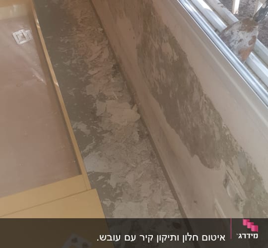 קיר מתקלף ליד חלון עם סימני רטיבות